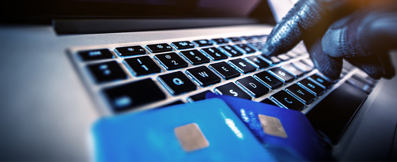 A gloved hand types on a laptop with two credit cards in the foreground